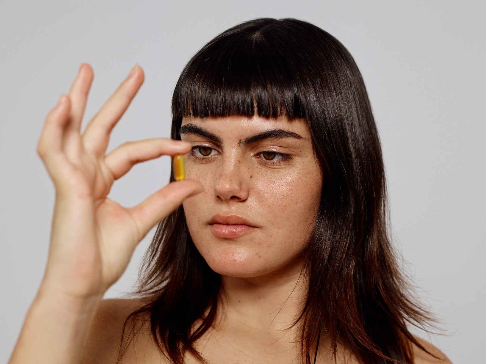 Femme aux cheveux mi longs tenant une gellule entre ses doigts et fixant l'interieur de celle-ci